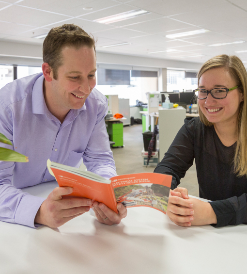 Man looking at a book while the woman next to him smiles for the camera