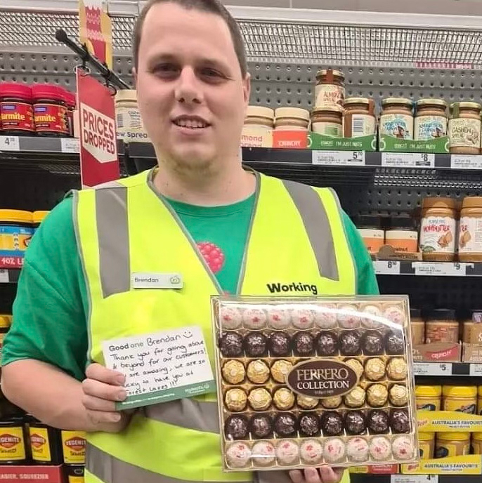 Brendan holding a box of chocolates and his 'Good One' form in an isle