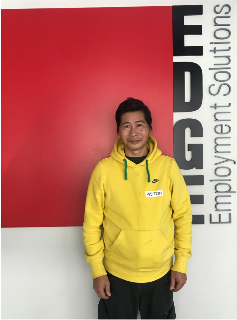 Van wearing a yellow jumper, standing in front of the Edge sign