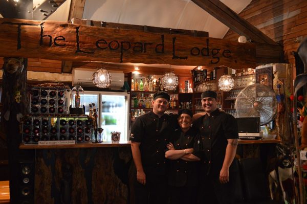 Three chefs standing in front of a bar with a sign- the Leopard Lodge