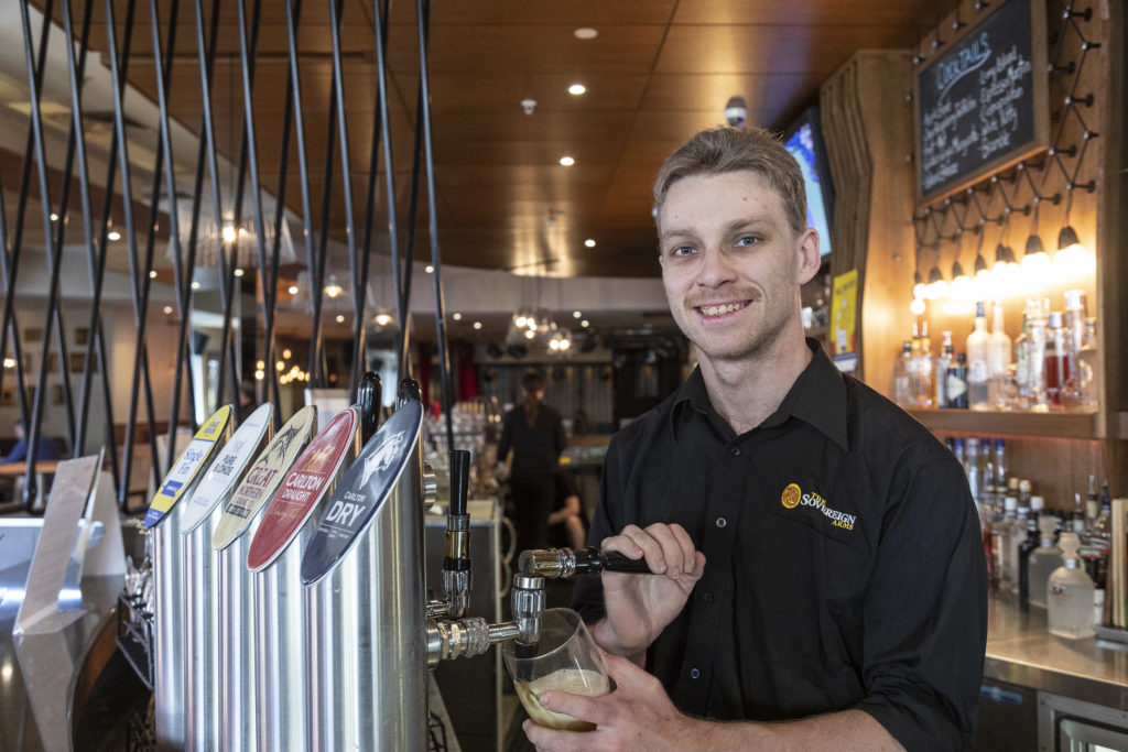 Alex smiling while standing behind a bar at work