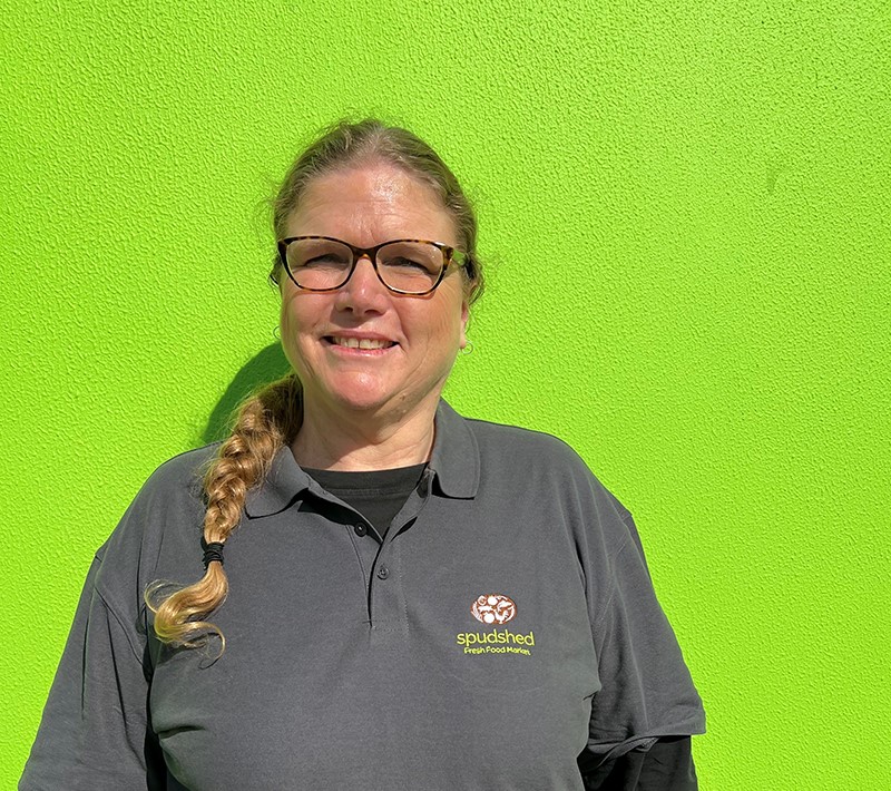 Jacqueline smiling in front of a lime green wall in her Spudshed work shirt.