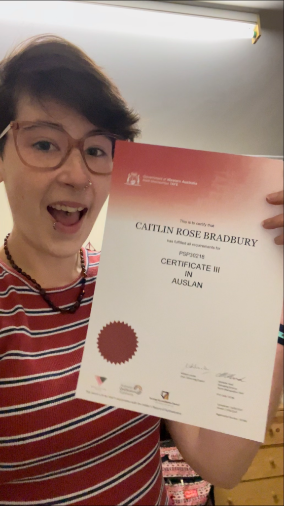 Caitlin holding her TAFE Certificate and smiling.