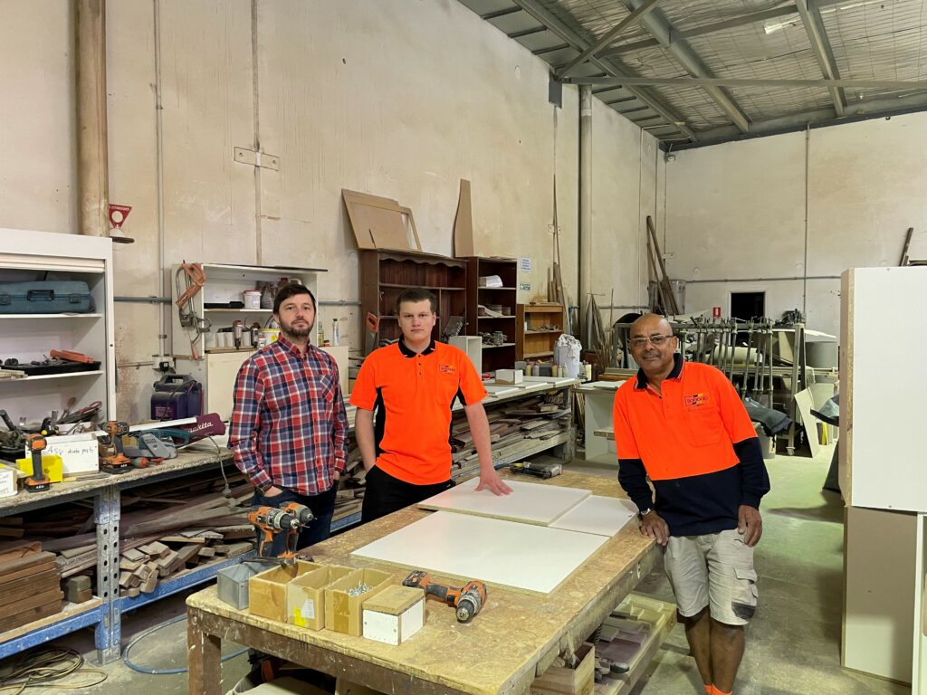 Three men standing together smiling in a workshop.
