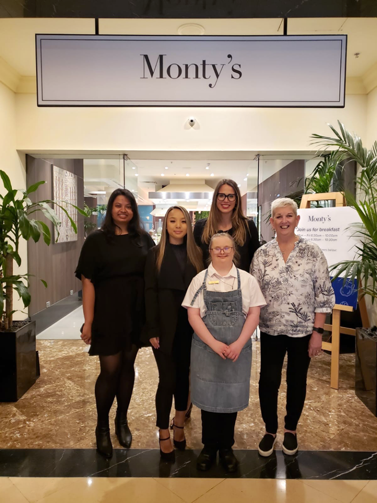 Five woman standing below a sign that reads Monty's smiling.
