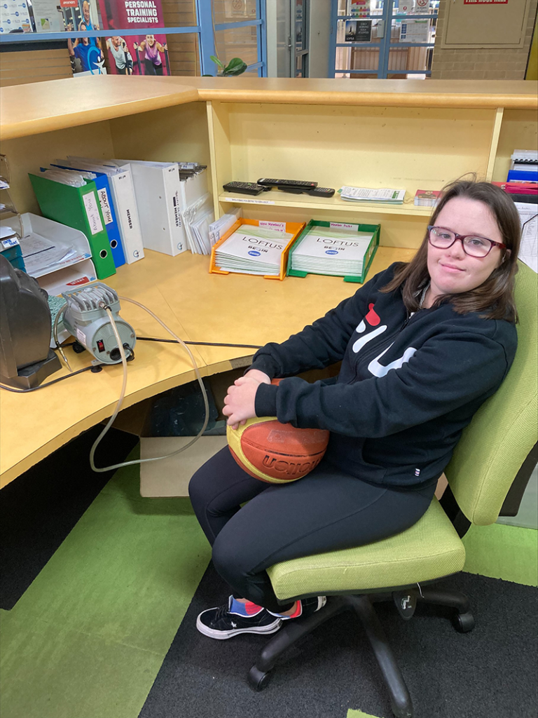 Sophia sitting on a chair smiling while holding a basketball.