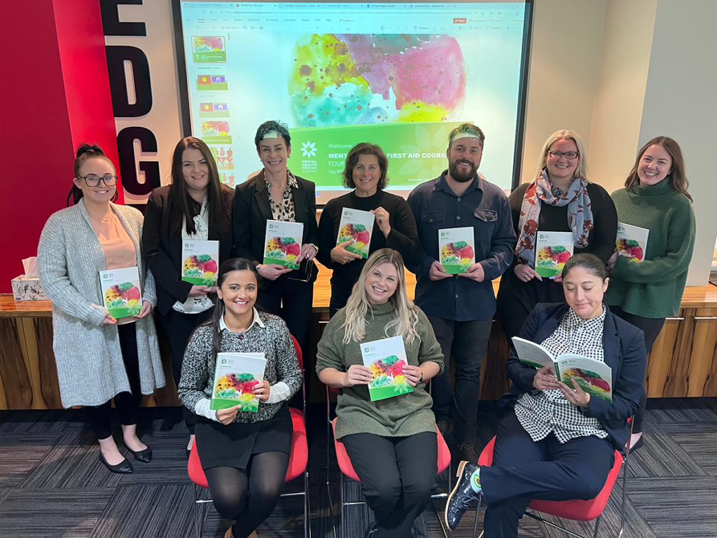 Group of Edge employees holding the Mental Health First Aid textbook and smiling.