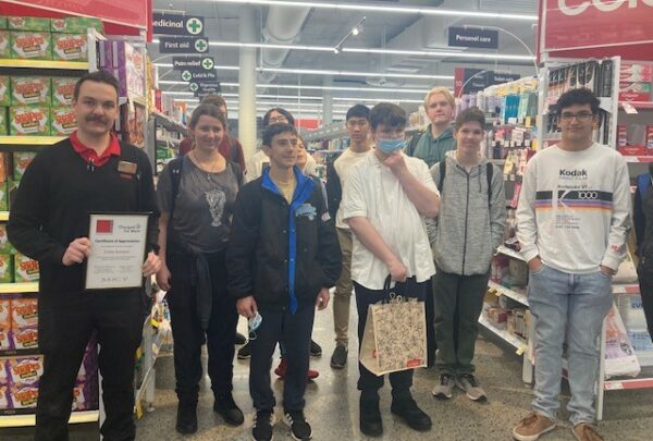 Group of students together standing beside a Coles Manager holding a framed certificate.