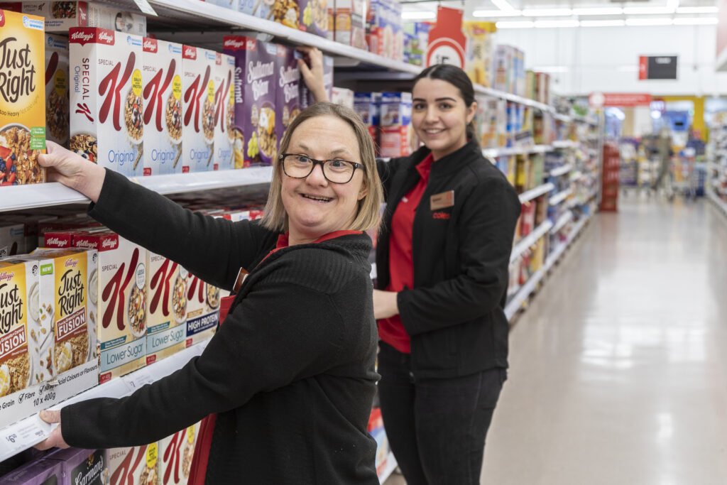 Linda smiling in front of her Coles Manager as they both reach towards items on a shelf.