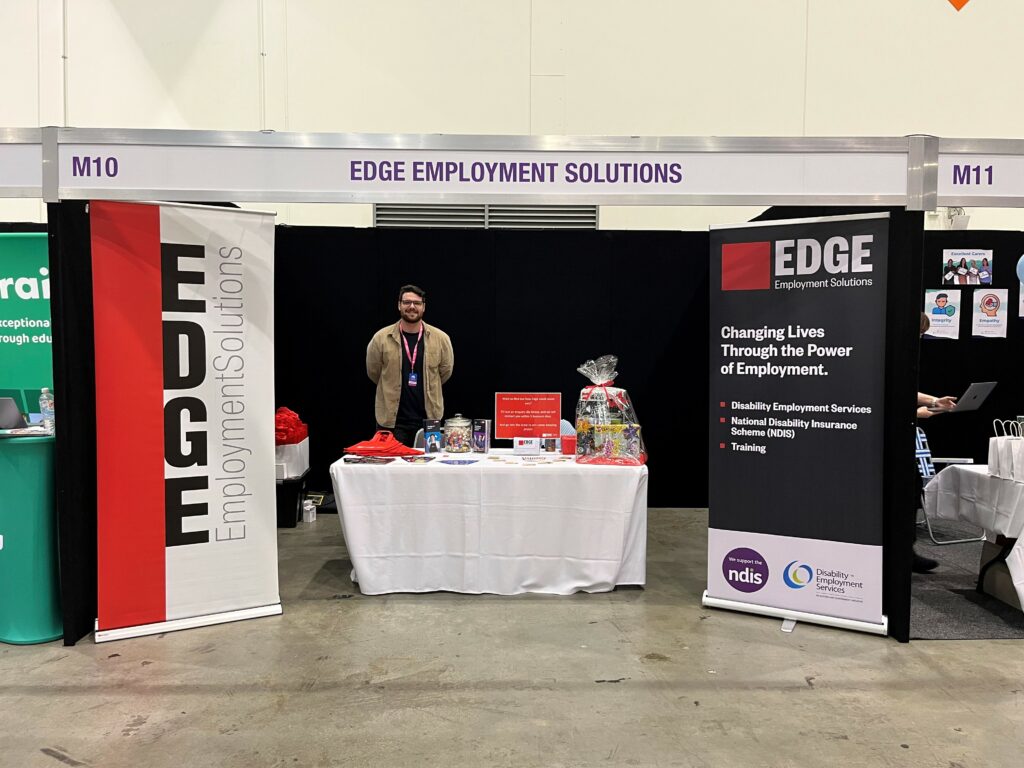 Edge expo stand with two banner signs and a desk with a man standing behind the desk
