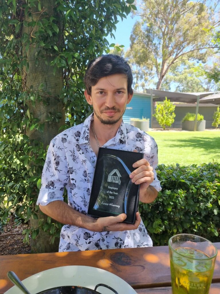 Louis sitting down holding a trophy with the Steel Frames WA logo and text reading, Employee of the Year 2023.