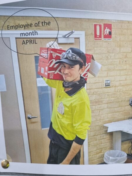 Printed image of Louis in his work uniform holding a carton of soft drink on one shoulder. There is a speech bubble with text reading, Employee of the month APRIL.