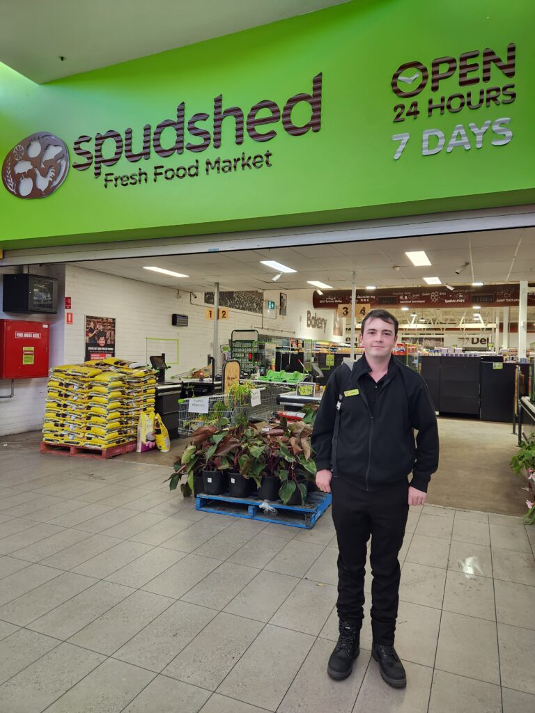 Cameron standing in front of the Spud Shed shop front smiling.