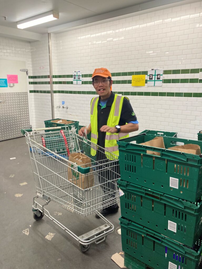 Eugene in a Woolworths t-shirt and high-vis vest smiling in front of a trolley.