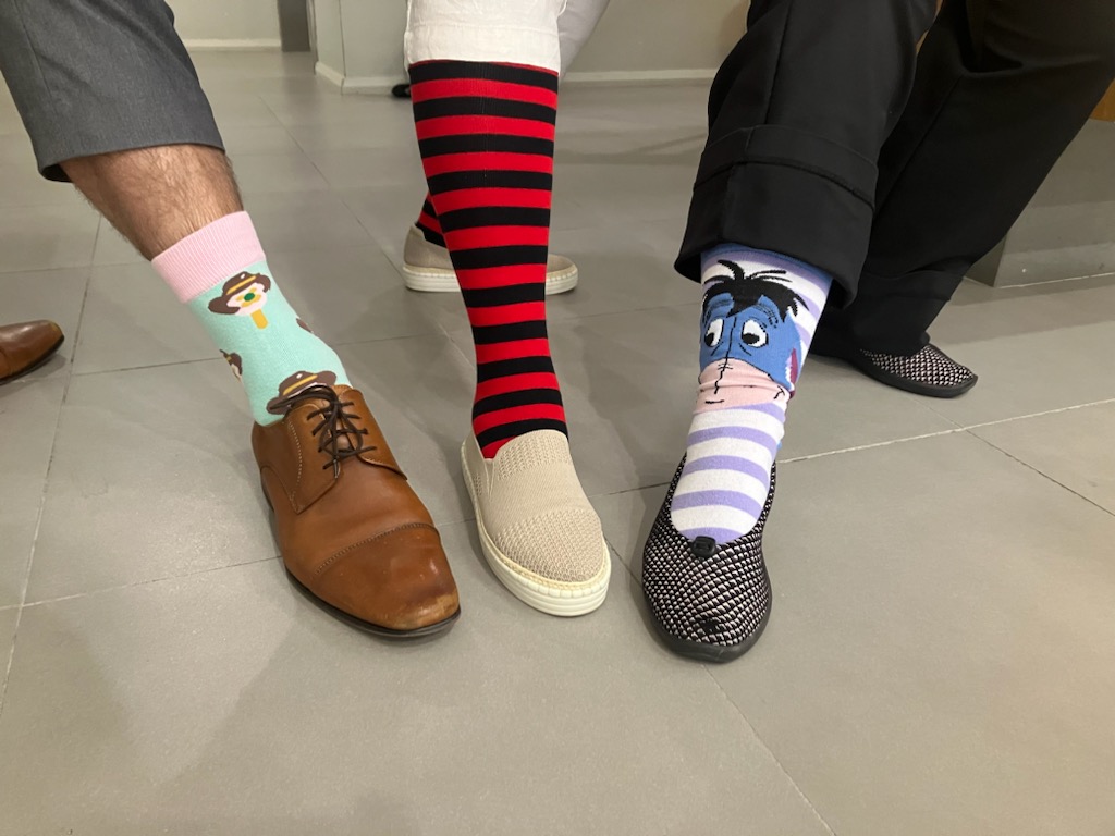 Image of three people's feet showing off their craziest socks. One is green and pink, the middle sock is red and black striped while the last one has purple and white stripes.