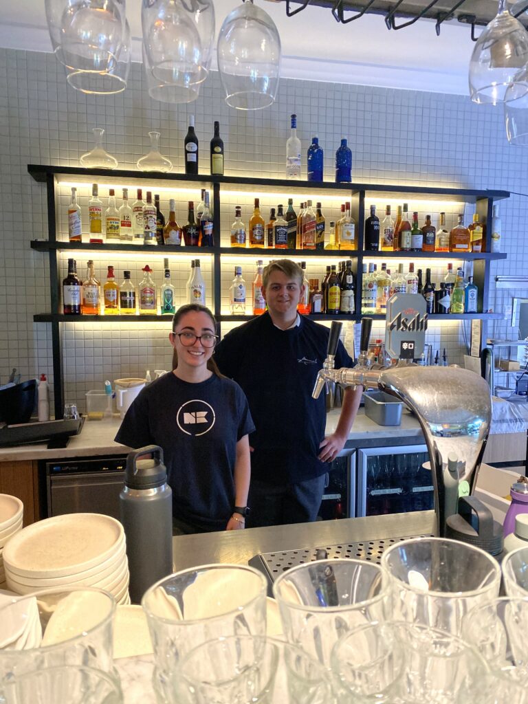 Two people standing together side by side behind a bar.
