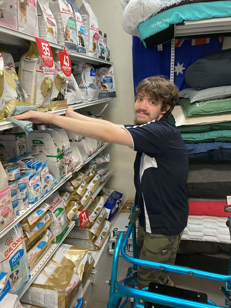Ryan standing in front of a shelf of pet food with his arms reached out wiping the surface.