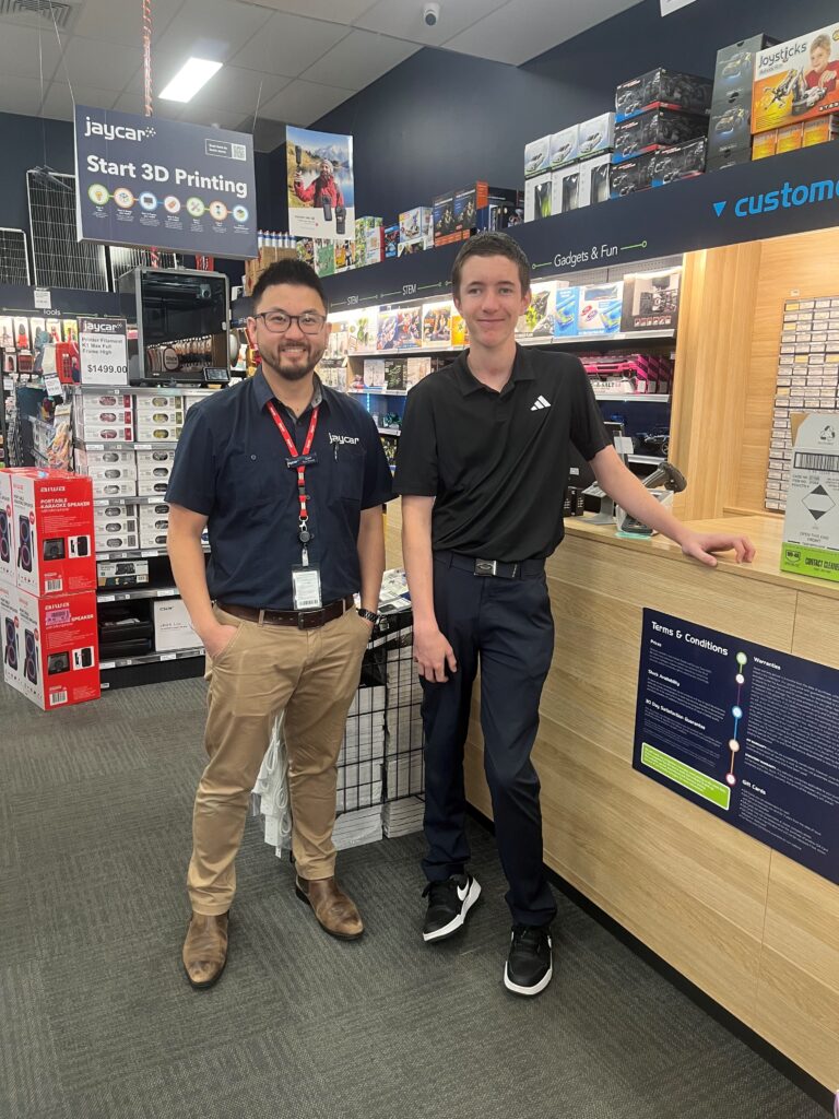 Two people standing side-by-side in front of a shop counter.