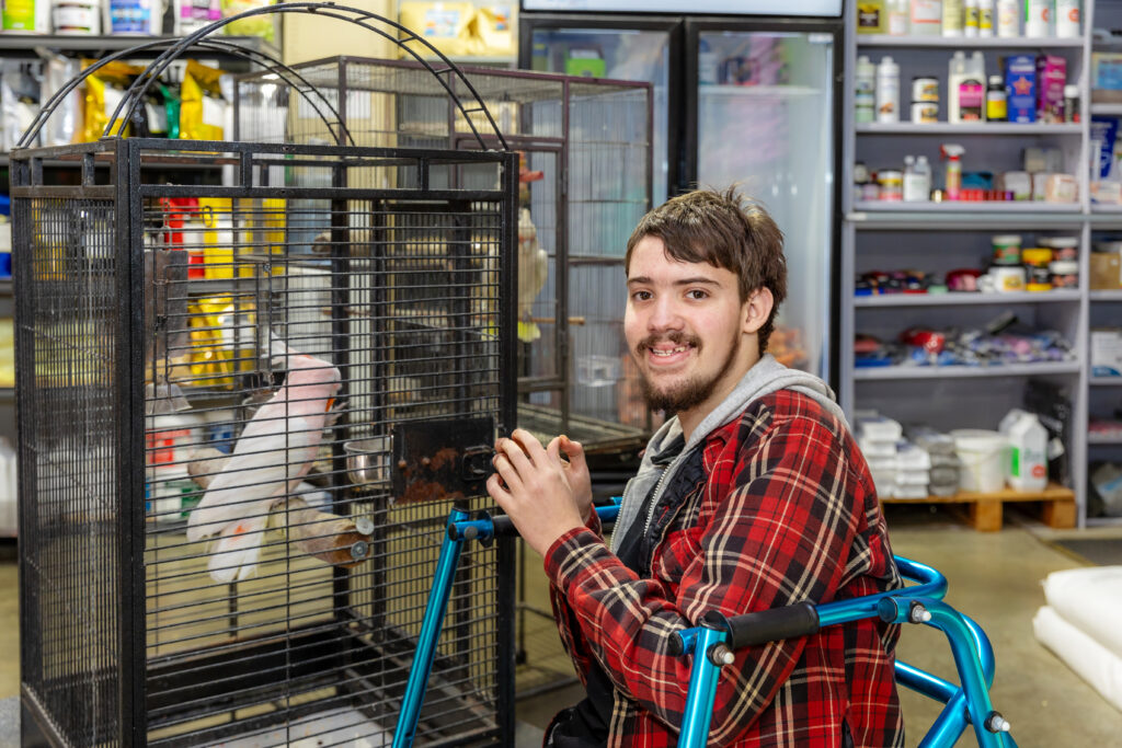 Mid shot of Ryan in front of a bird cage with a bird in the cage.