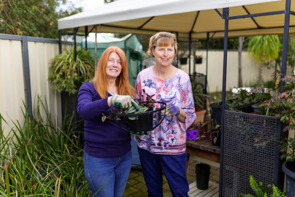 Two women smiling and holding a potted plant while gardening together, representing inclusive employment support through Edge.