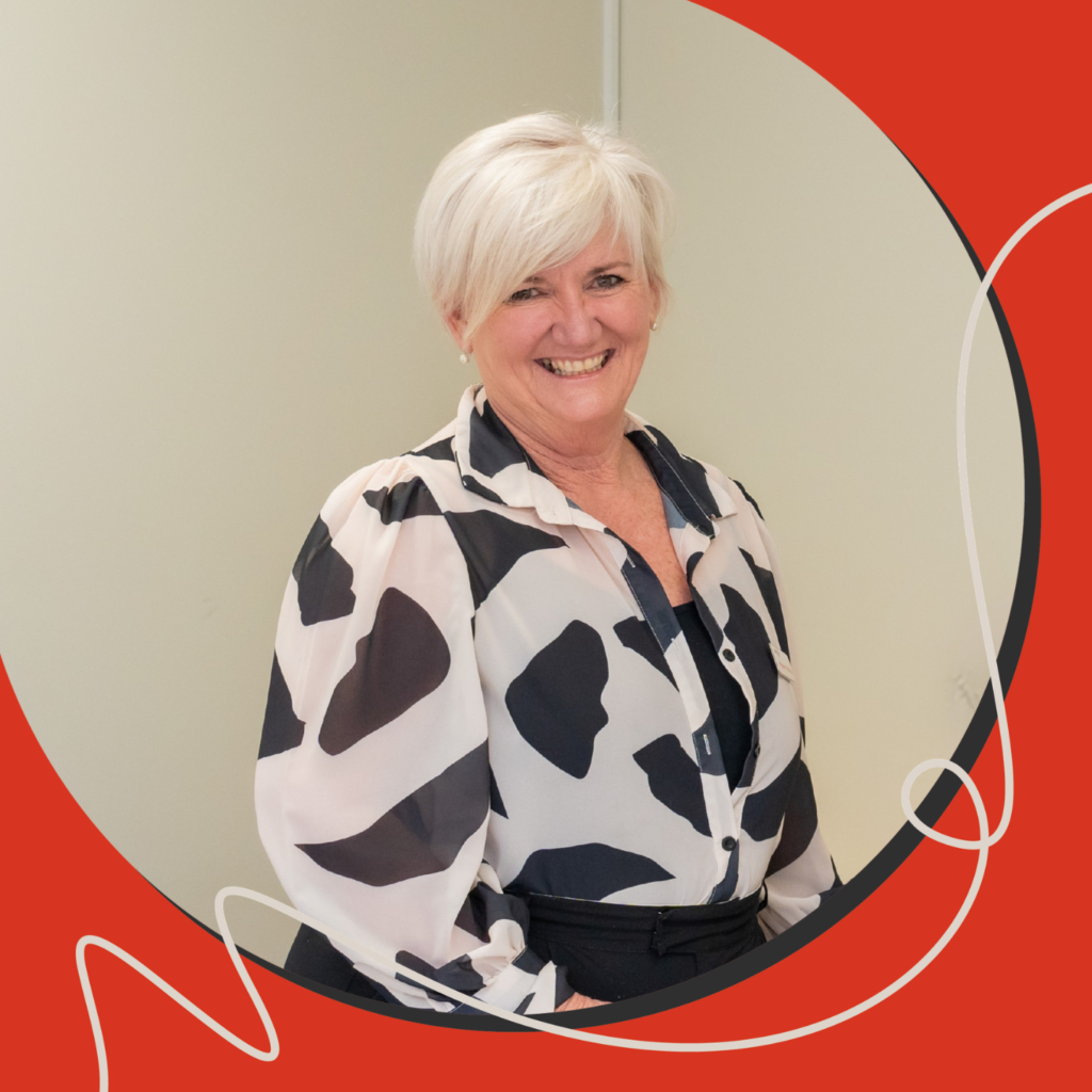 A woman smiling with short hair. She is wearing a black-and-white patterned blouse, standing against a neutral wall with a red graphic border over the image.